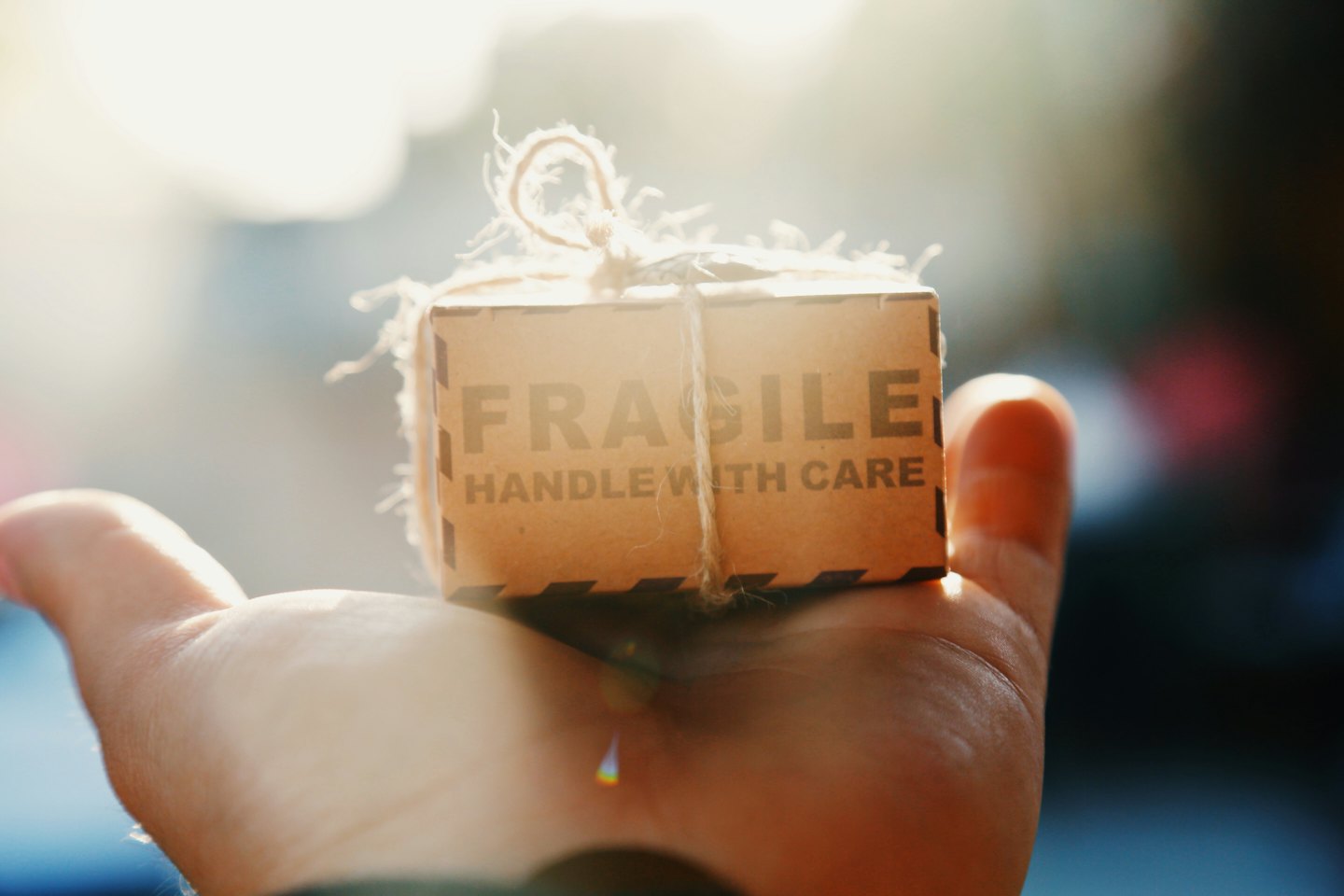Main tenant une petite boîte brune marquée « FRAGILE ».